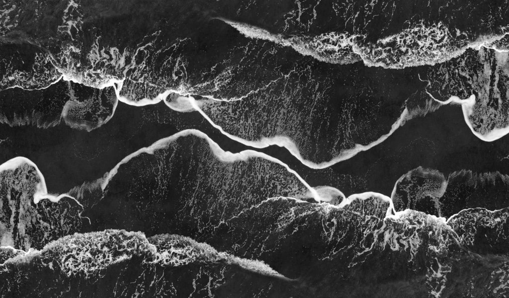 Stunning monochrome aerial shot of ocean waves crashing on the shore, creating abstract patterns.